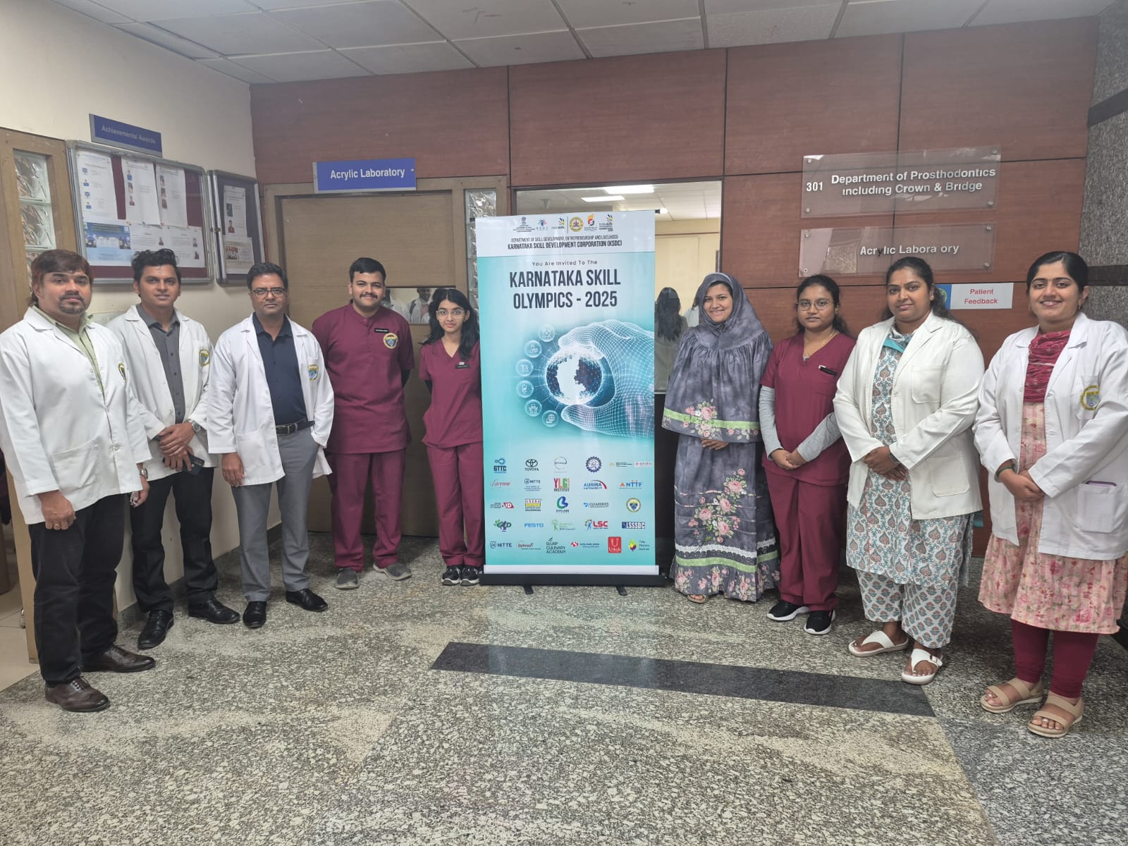 Faculty and students standing next to the Karnataka Skill Olympics 2025 banner in the department